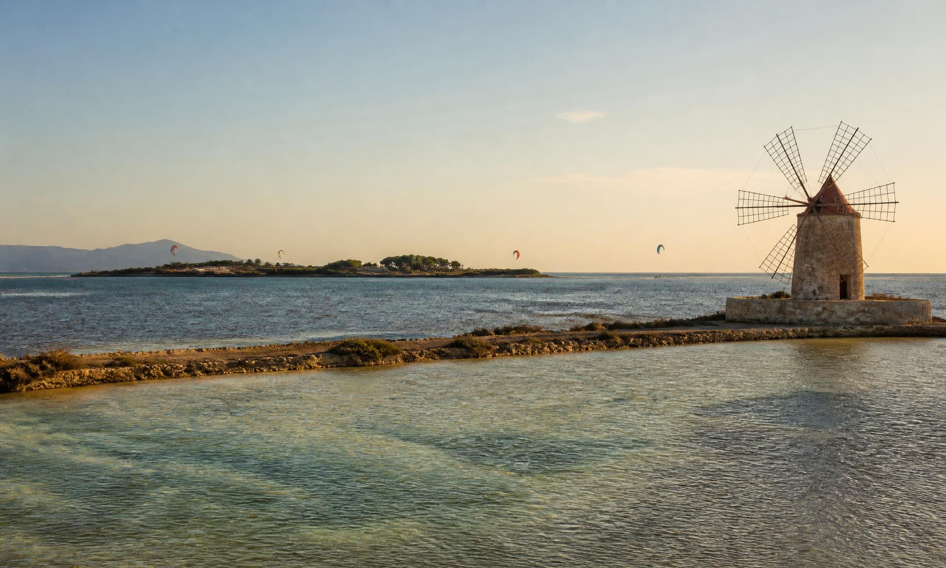 The Lo Stagnone lagoon at golden hour with Mozia island, a stone windmill and distant kites